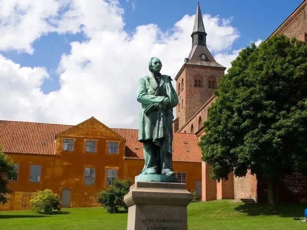 Bronze statue of Hans Christian Andersen in Odense, Denmark, with a church tower in the background