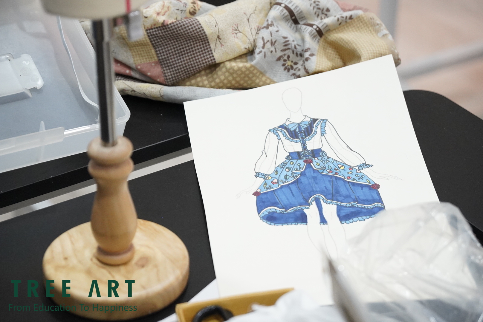 Fashion-design illustration of a blue dress beside a dressmaker stand and patchwork fabric