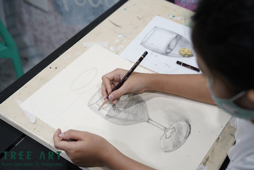 Child sketching a still-life wine glass in pencil during a drawing class