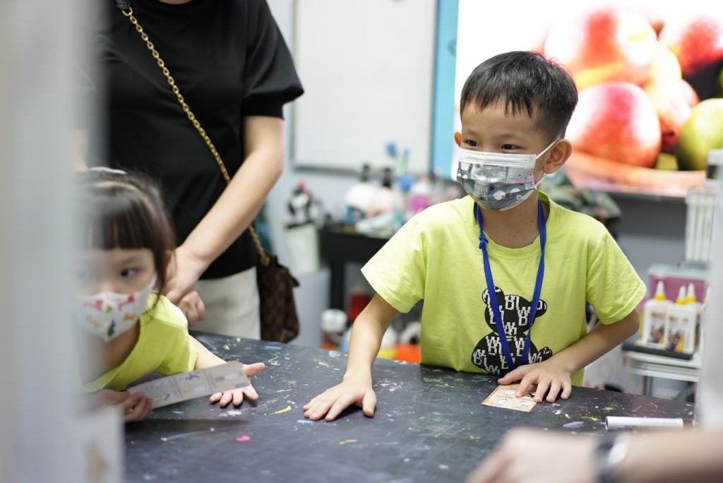 Two children in matching art class T-shirts standing at a classroom table