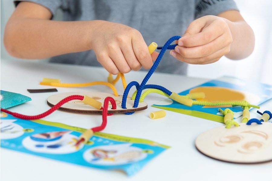 Child's hands threading coloured cords through a wooden lacing card to build fine motor skills