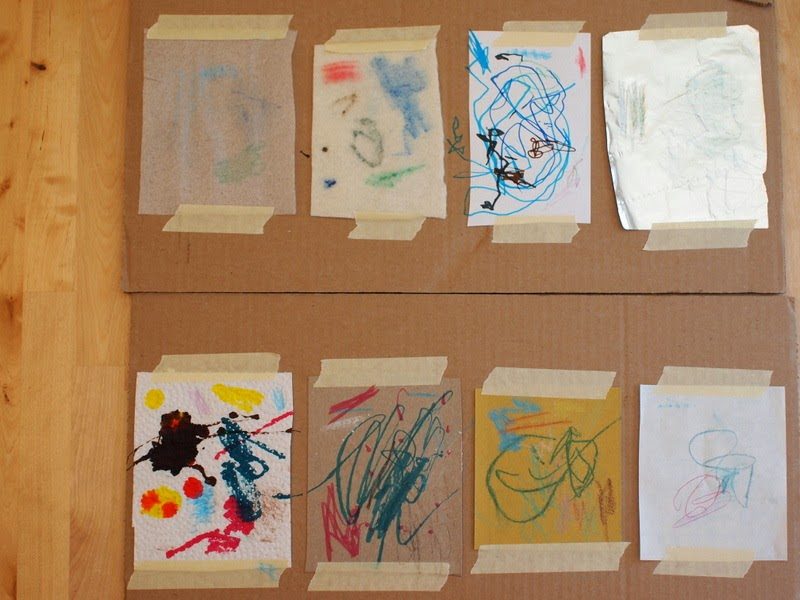 Children's drawings and paintings made on different materials such as paper, fabric and foil, taped to a board