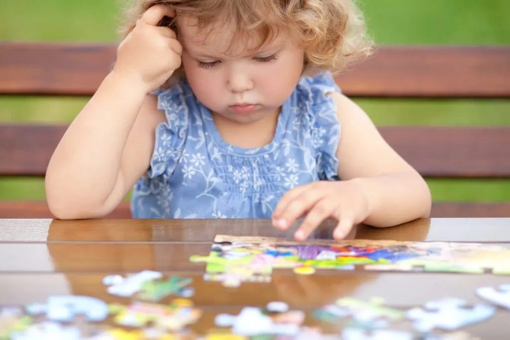 A young child concentrating while solving a jigsaw puzzle outdoors
