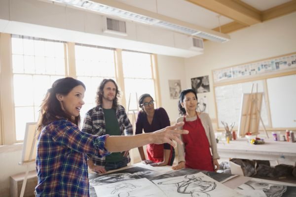 An art instructor guiding a small group of students around sketches laid out in a studio