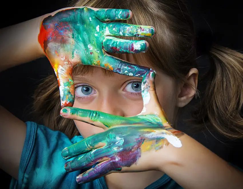 Close-up of a child framing her face with paint-covered hands