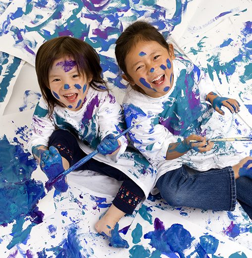 Two girls laughing while covered in blue and purple paint during a hands-on painting session