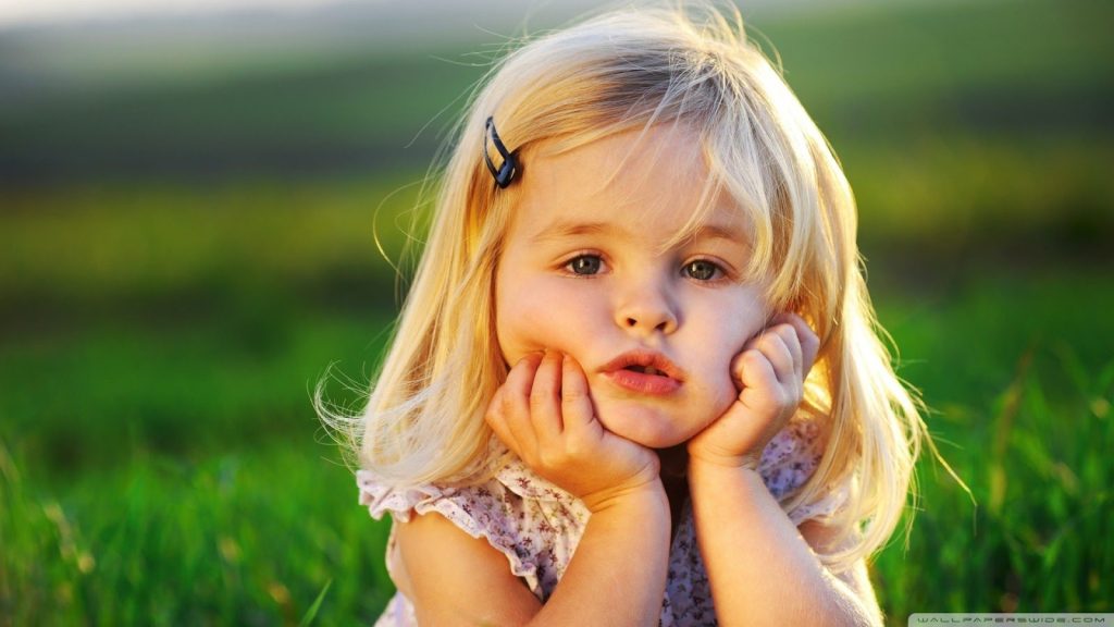 Young girl resting her chin on her hands in a grassy field, capturing childlike wonder