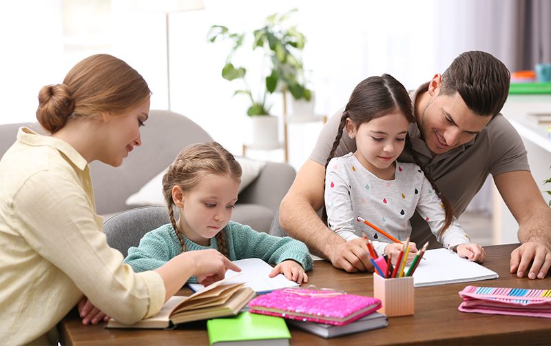 Parents sitting with two young daughters, encouraging them as they draw with colored pencils at home