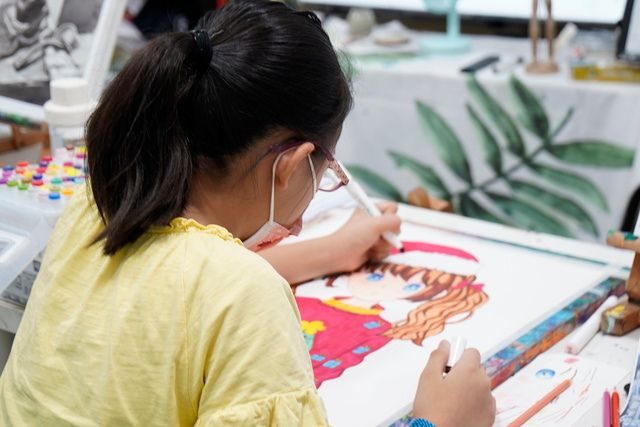 Girl wearing glasses and a face mask carefully colouring a character drawing