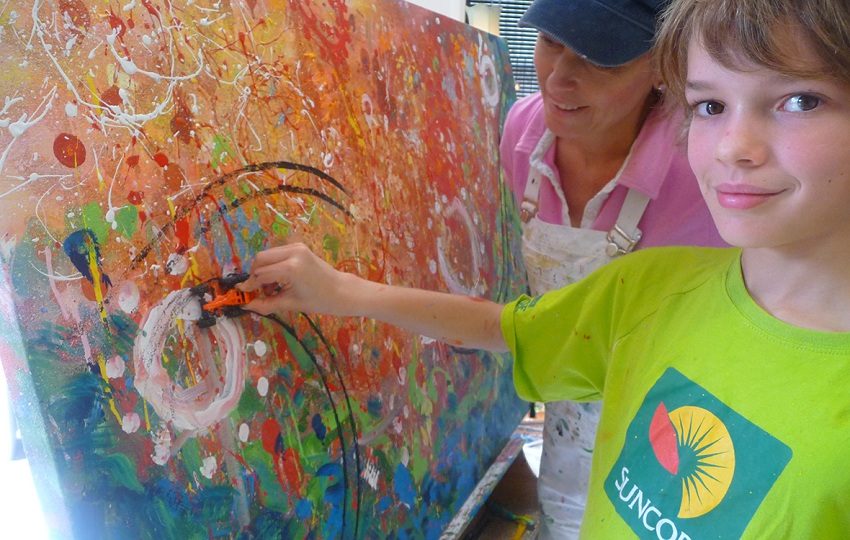 Smiling boy painting on a large abstract canvas beside his art teacher