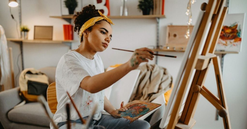 Young artist calmly painting at an easel in a cosy home studio
