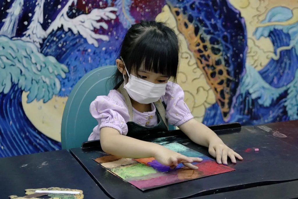 Young girl in an apron carefully blending coloured pastels on paper during an art class at Tree Art