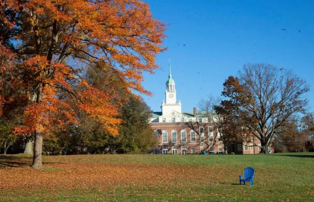 Autumn scene on an Ivy League campus with a clock tower building and an empty blue chair on the lawn