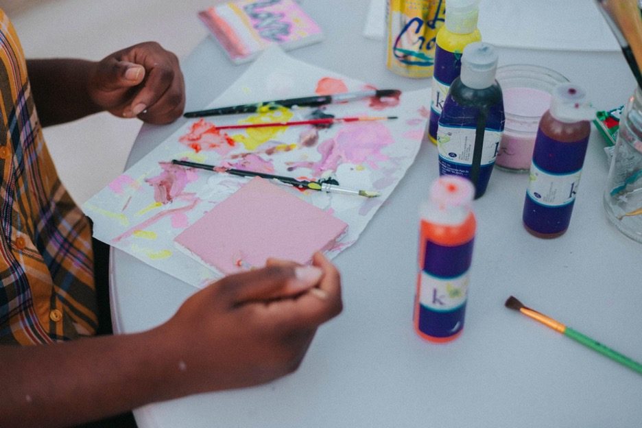 Close-up of hands mixing paint colours on paper, surrounded by brushes and paint bottles