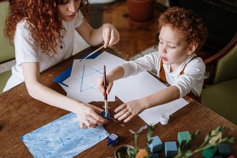 An adult guiding a child through a painting exercise, tracing a star shape in blue paint