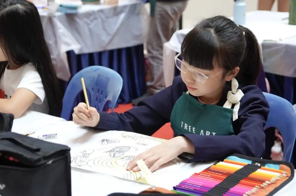 A young girl wearing a Tree Art apron concentrating on a drawing at an art class table