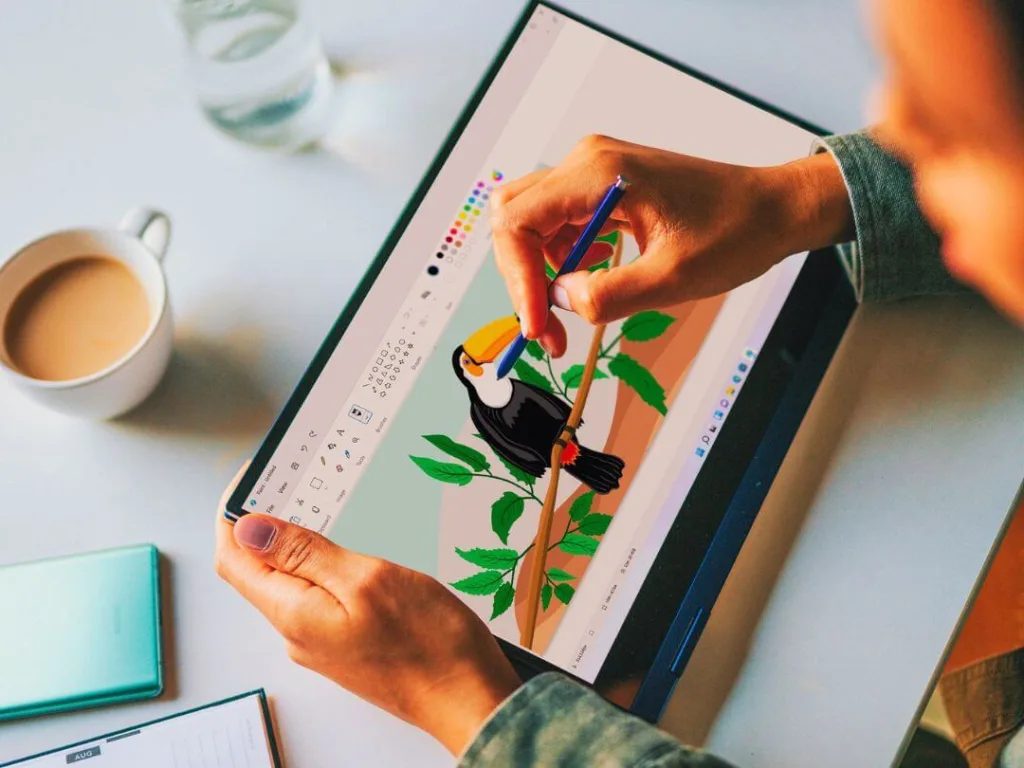 Hands drawing a toucan illustration with a stylus on a digital tablet