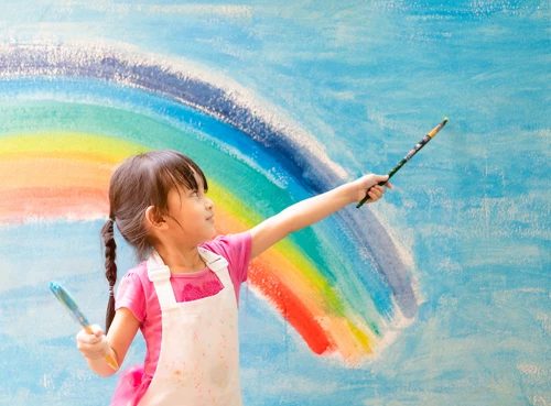 A young girl painting a colourful rainbow mural on a wall