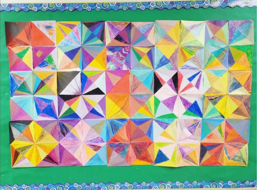 A colourful collaborative mosaic artwork made of individually decorated paper squares displayed on a classroom board