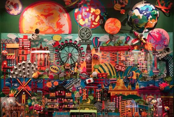 An elaborate 3D paper-craft mural made by TreeArt students, featuring planets, hot air balloons, and landmarks from cities around the world