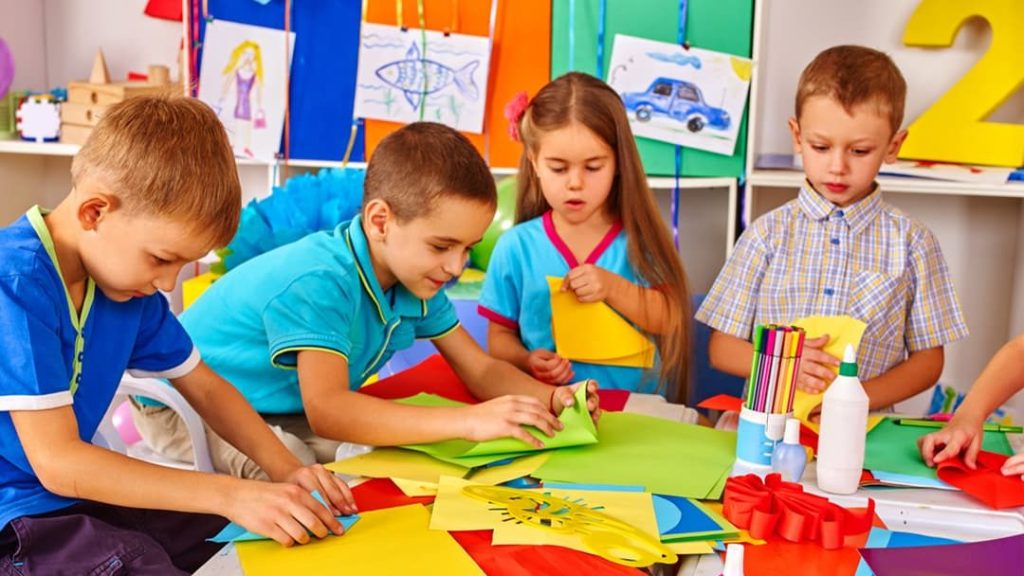 Group of children working together on a colorful paper craft project at a shared table