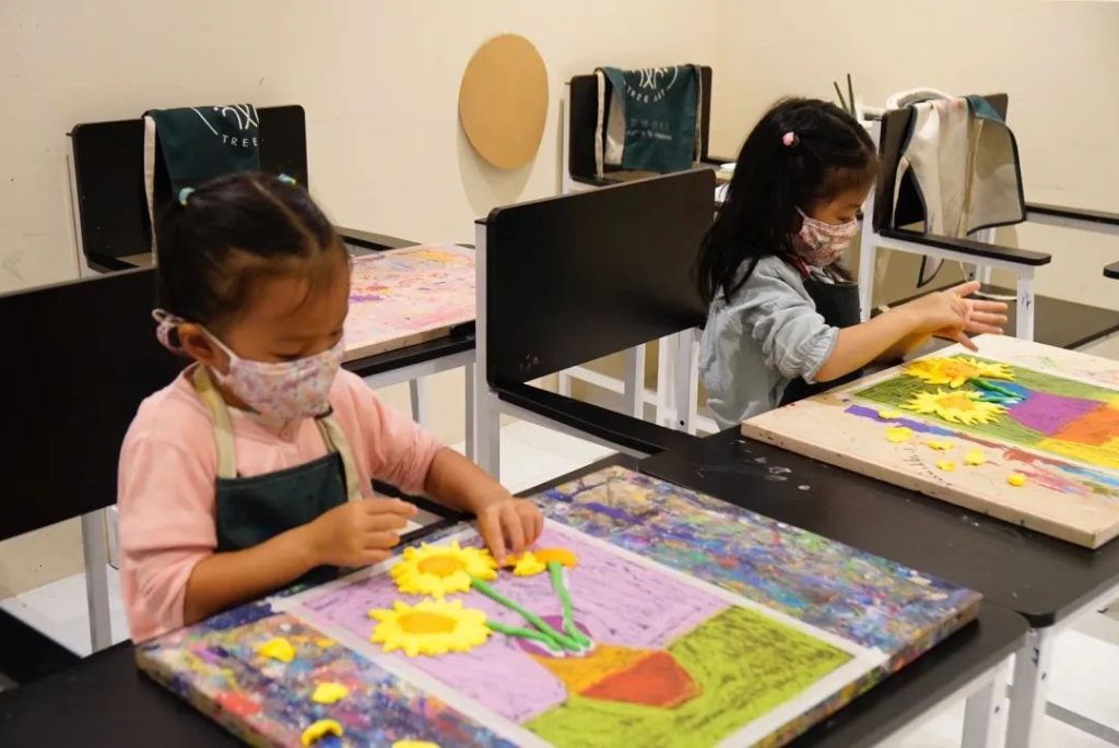 Children shaping colorful clay sunflower petals onto a mixed-media canvas