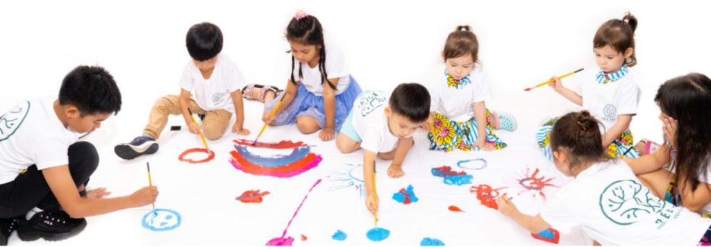 A group of children in Tree Art T-shirts painting together on a large shared canvas
