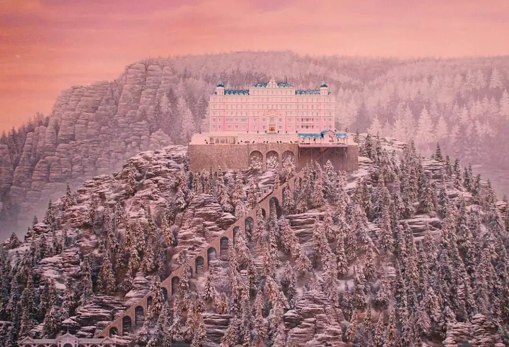 Still from The Grand Budapest Hotel showing the hotel perched among the mountains in a symmetrical composition