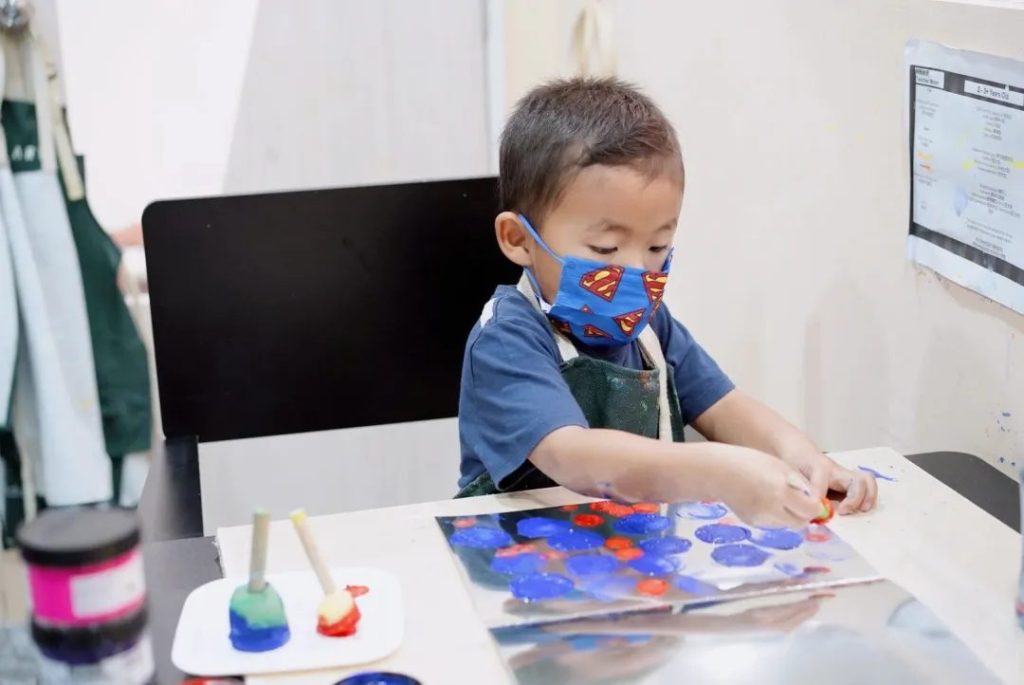 A young boy freely stamping circles of paint with sponge daubers
