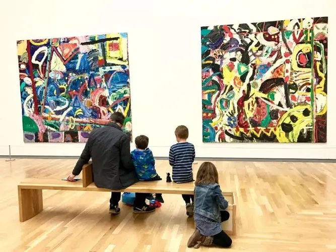 A parent and three children sitting together admiring large abstract paintings in a museum