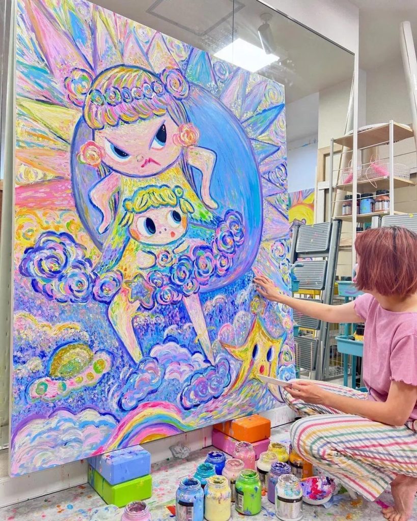 Bibi Lei painting a large canvas with her fingers, bringing to life two whimsical pastel-colored girl characters