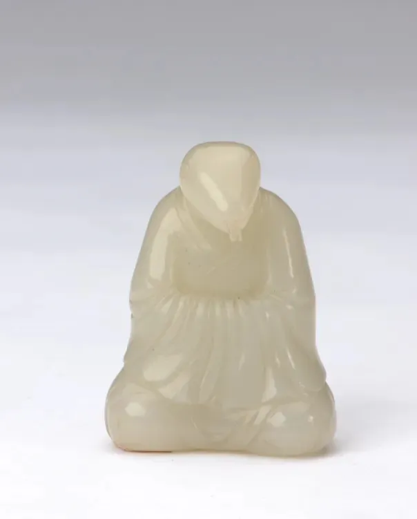 Pale jade carving of a seated robed figure with a smooth, rounded head, displayed as a museum artifact