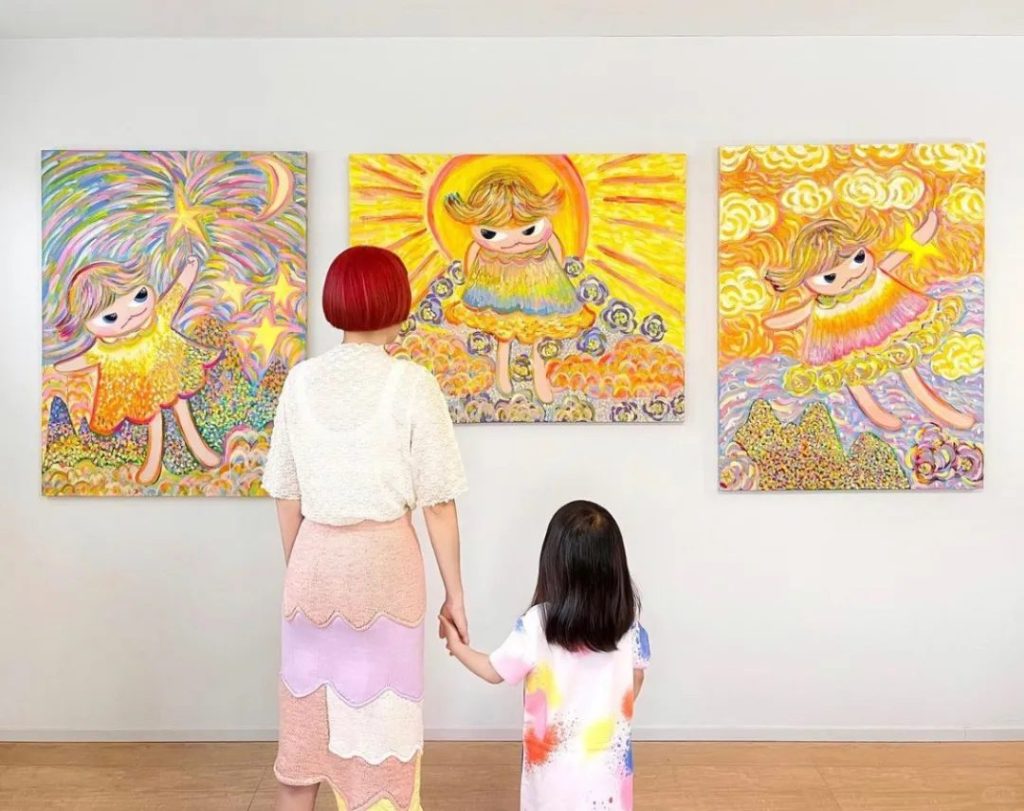Bibi Lei and her daughter holding hands while viewing three of her paintings in a gallery
