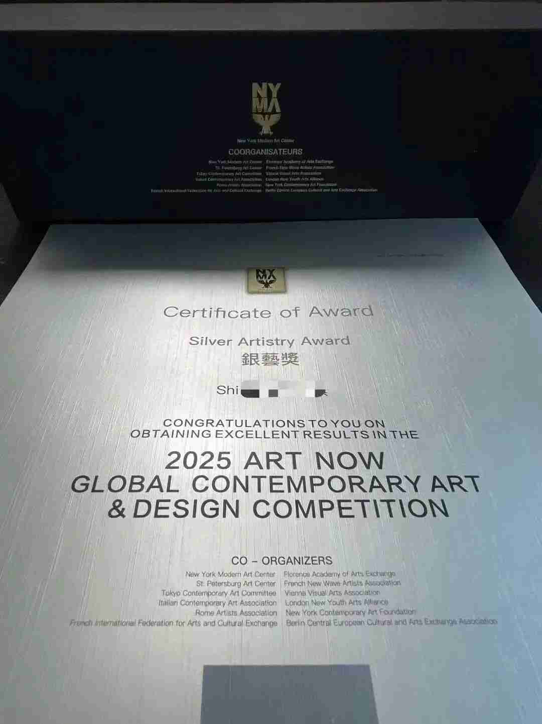 Sample Silver Artistry Award certificate displayed in its presentation folio with co-organizer logos