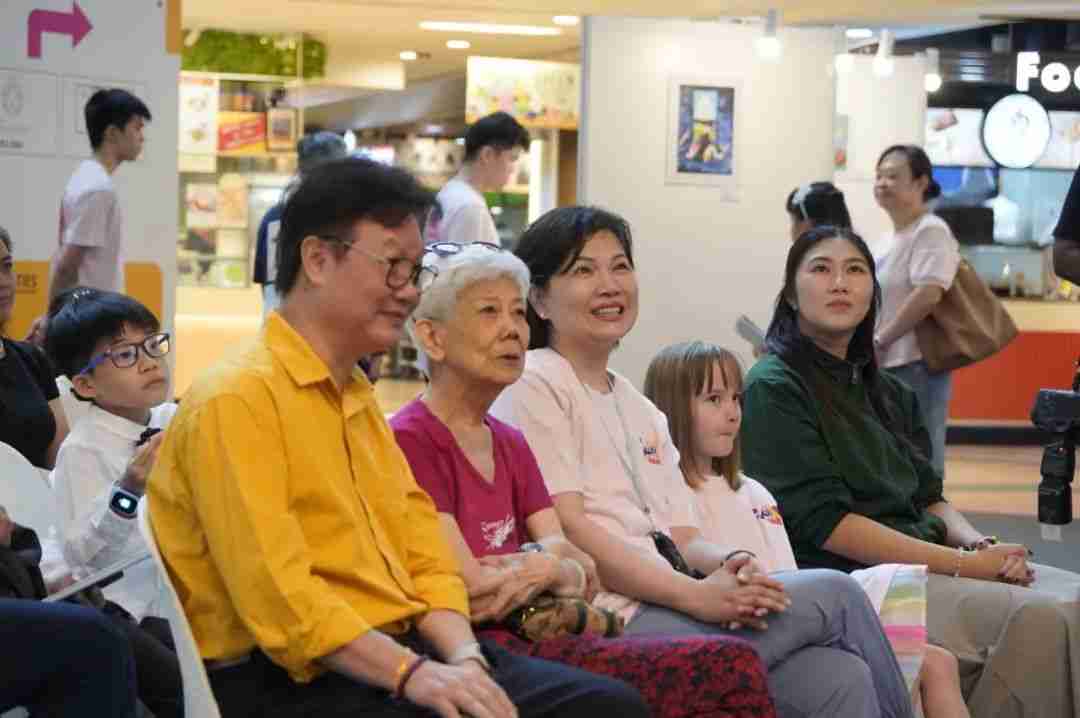 Guests and young participants seated in the audience at the World Without Cancer award ceremony, with framed competition artworks displayed on the wall behind them