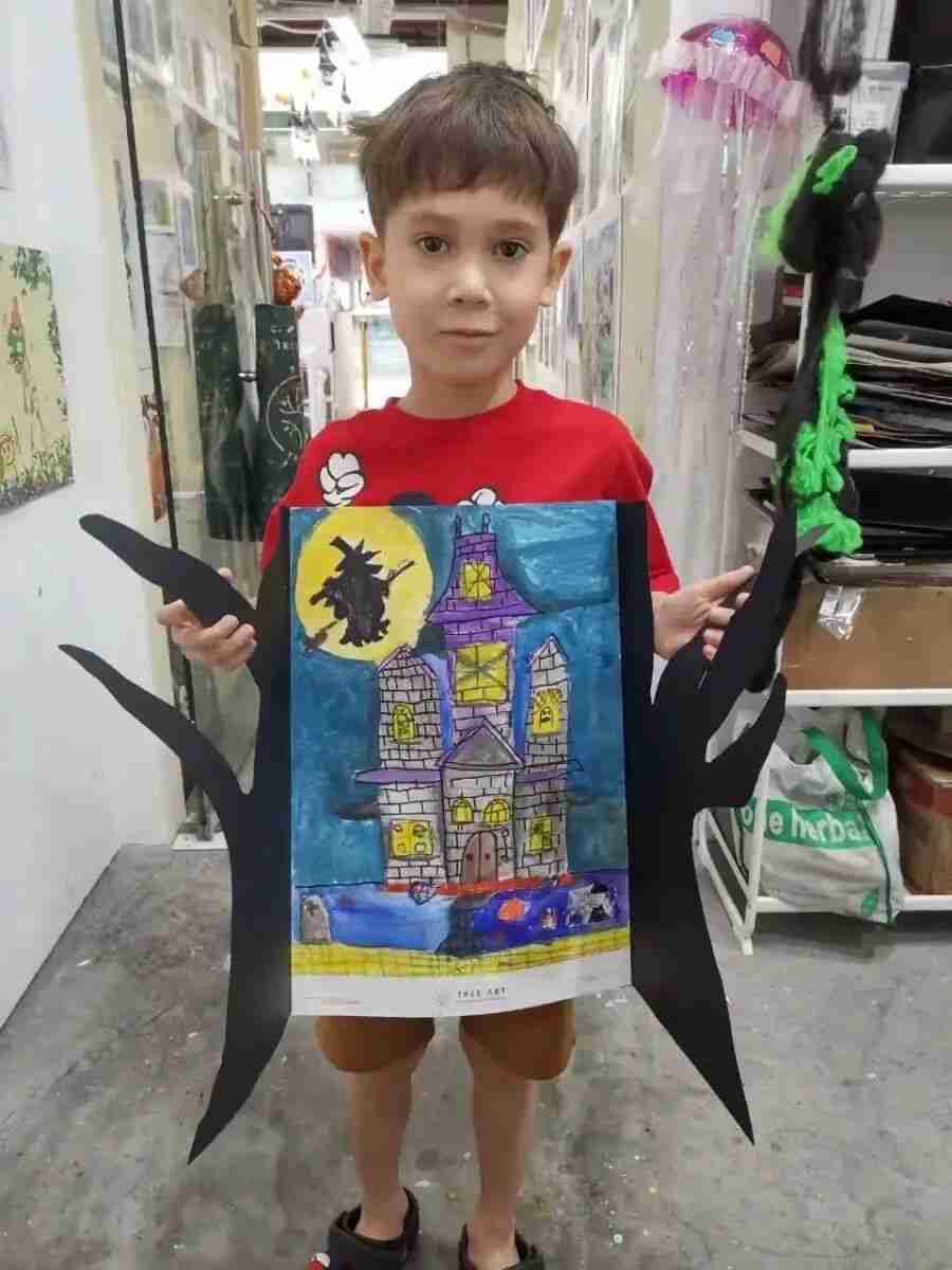 A TreeArt student holding his Halloween-themed haunted house painting