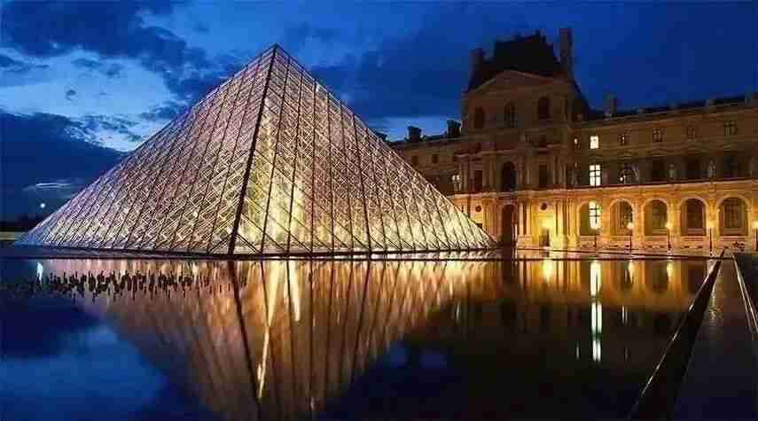 The Louvre Pyramid illuminated at night, reflected in the courtyard fountain