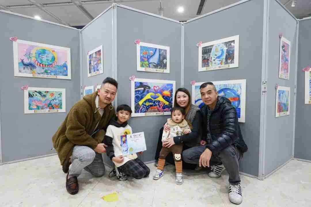 Family posing with a child's award certificate in front of exhibited children's paintings at the art festival exhibition