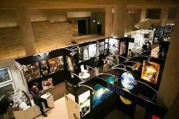 Overhead view of an exhibition hall with artworks displayed on partition walls and visitors browsing