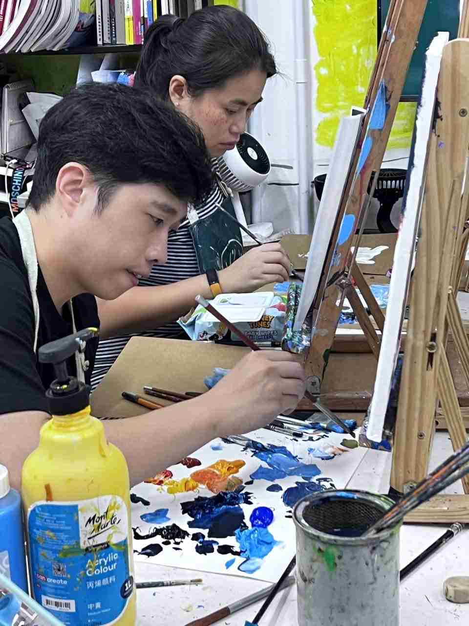 Two adult students concentrating on acrylic paintings side by side at easels