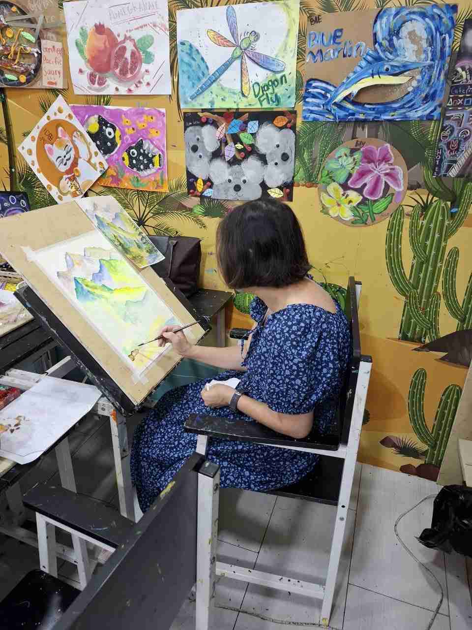 Adult student painting a watercolour mountain scene at a tilted drawing board
