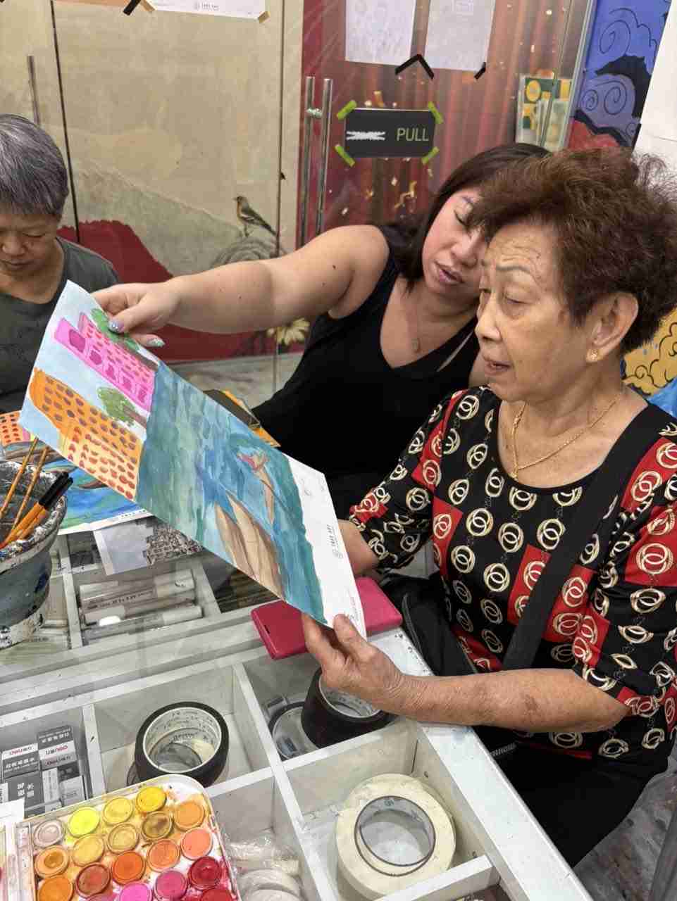 Two seniors admiring a finished watercolour of boats and colourful buildings