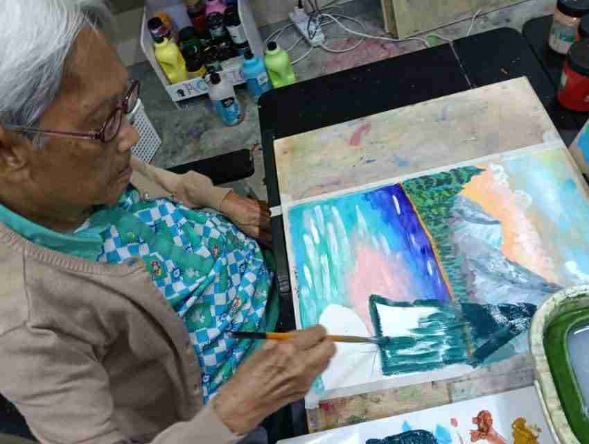 Elderly student painting a mountain landscape in acrylics