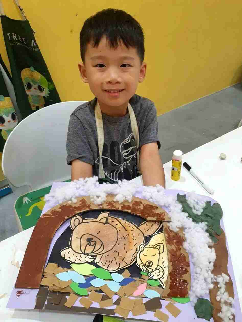 A TreeArt student smiling while holding up his mixed-media artwork of bears in a den