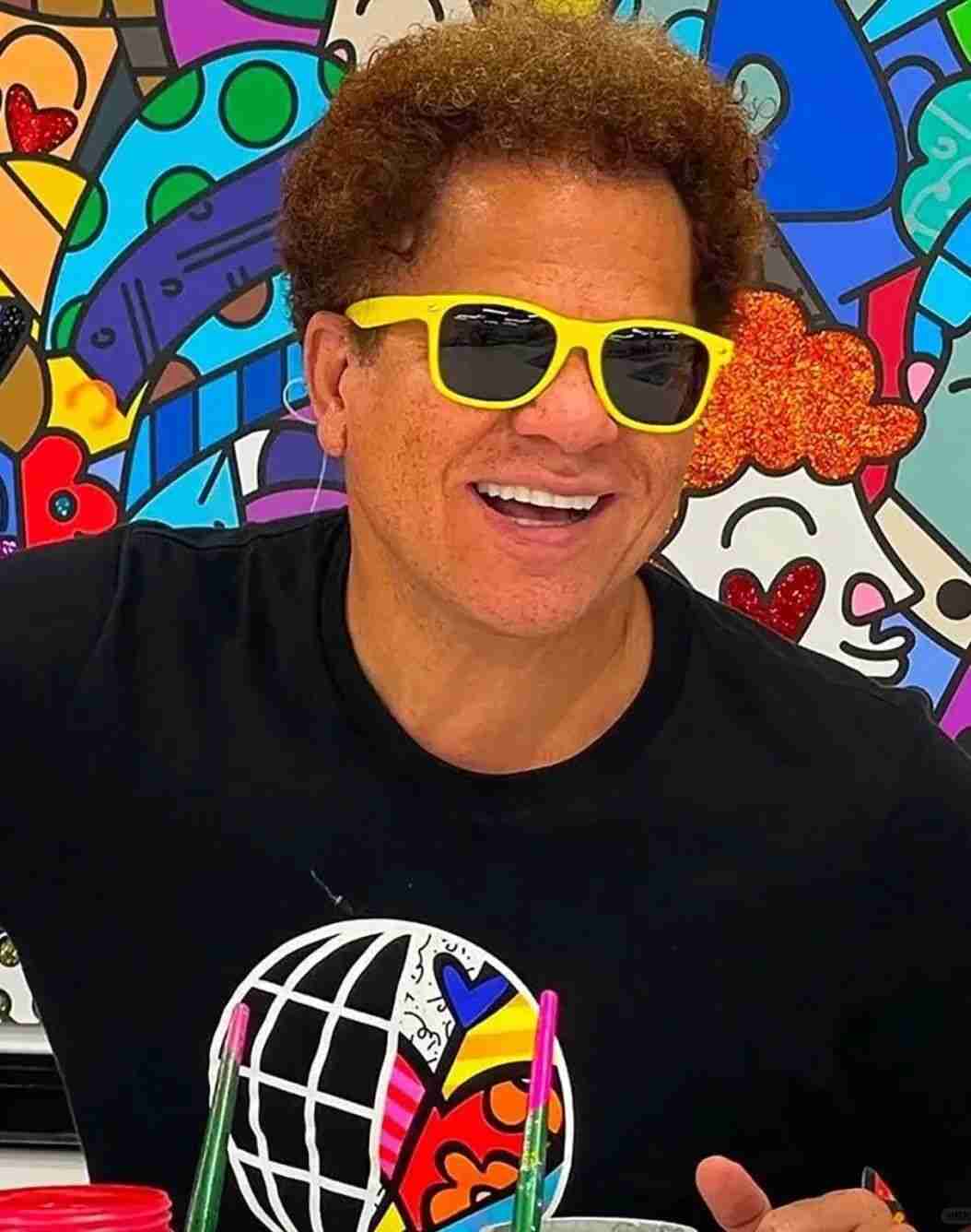 Romero Britto smiling in yellow sunglasses in front of a colourful mural