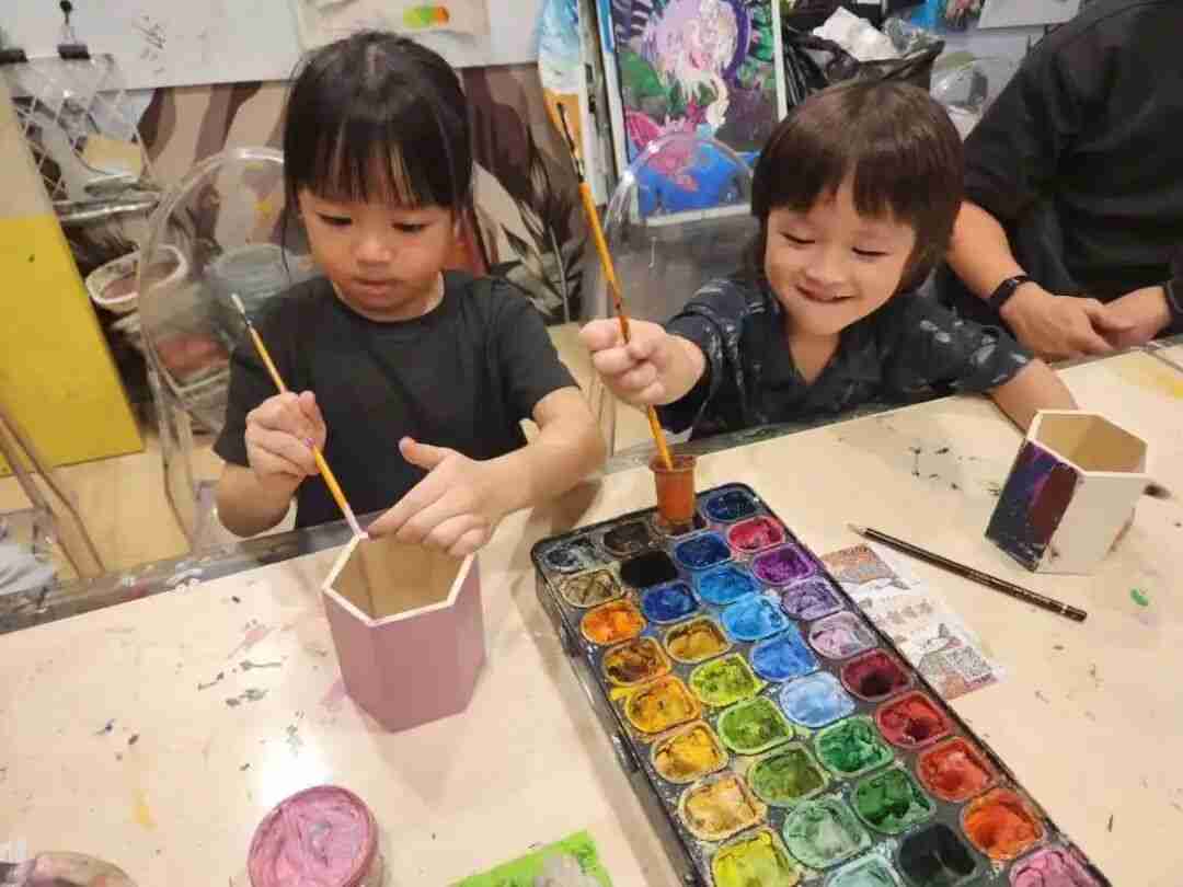 Two TreeArt students painting hexagonal pen holders together in Team Creation class