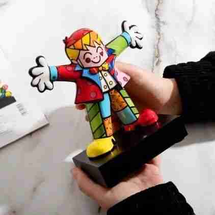 A small Britto figurine of a boy with open arms, painted in bright patchwork patterns