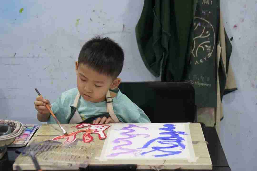 A young boy in a TreeArt apron painting flowing swirls of colour with a brush