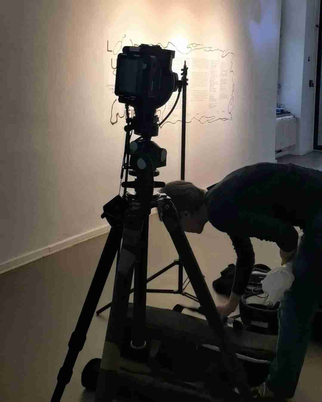 Photographer setting up a large-format camera in front of a wall-text artwork during installation at Kunstquartier Bethanien