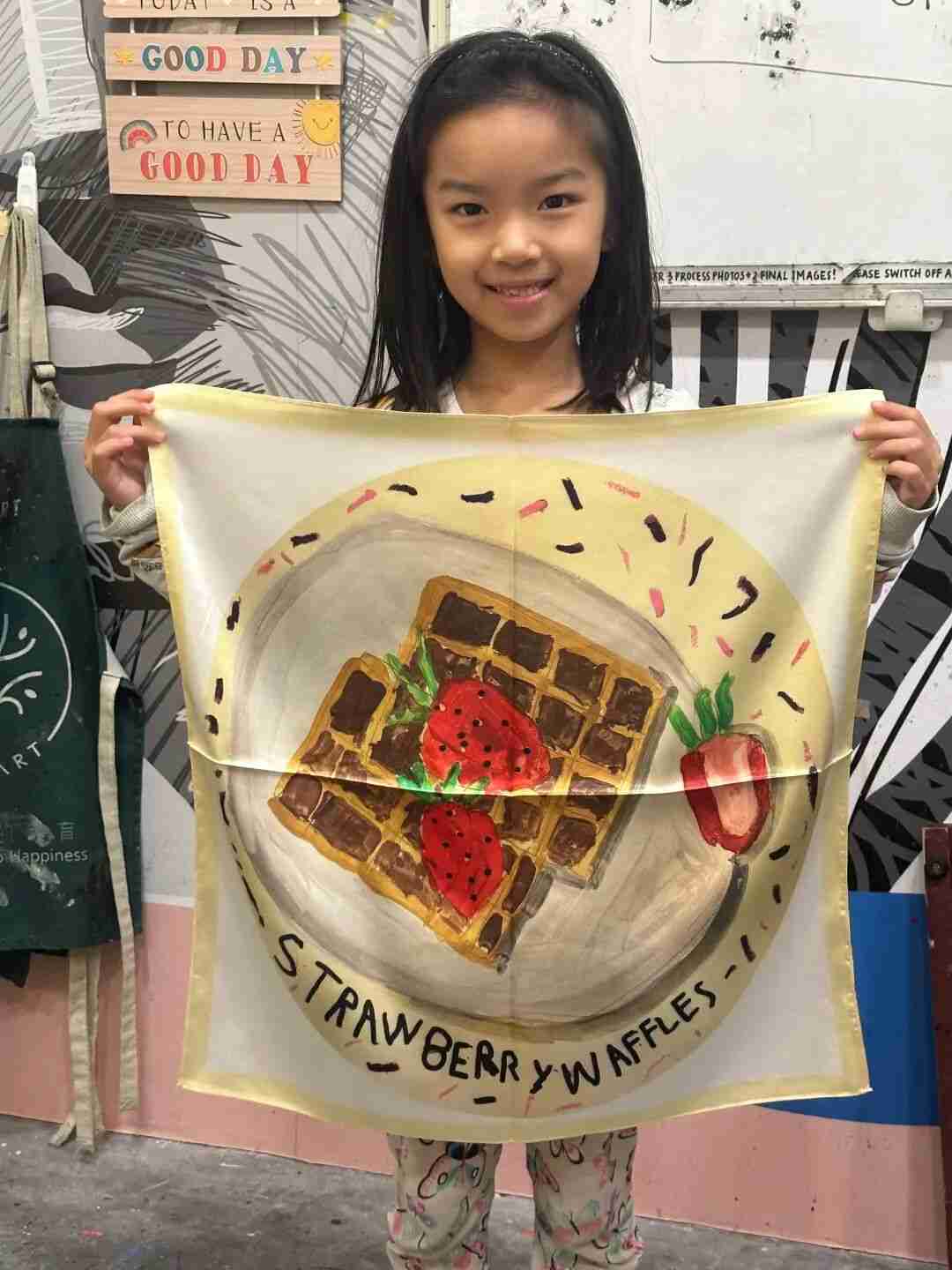 Child holding a silk scarf featuring their own painted pattern